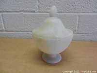 Front angle of hand carved alabaster jar with rounded body and pedestal base, topped with fitted domed lid with finial.