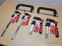 Photo of six clamps arranged on table showing two 12 inch Bessey bar clamps, two 6 inch Bessey bar clamps, and two Husky C-clamps