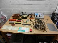 Overview of a collection of vintage model train items on a table, showing locomotives, power supplies, track, wires, and manuals.