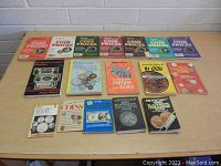 Front view of all 15 vintage coin collecting and pricing books on a wooden table against a white brick wall.