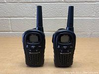 Front view of two black Midland walkie talkies standing upright, showing front face with screens and buttons.
