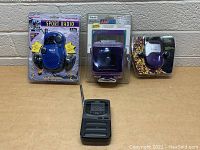 Four electronic items: blue Sport Radio with earphones, portable AM/FM radio, small purple device in packaging, black handheld device with antenna out of packaging.