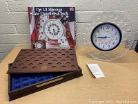 Clear circular clock with white face and black numbers is shown with original box and instruction sheet behind. Wooden presidential coin case with recessed slots in front.