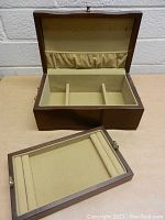 Open wood jewelry box showing beige velvet interior with multiple compartments and removable tray in front.