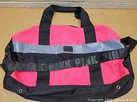 Front angle of pink and black Victoria's Secret PINK tote bag showing reflective strip and black handles with long black shoulder strap with PINK logos.
