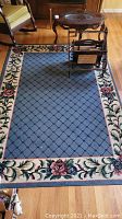 Full view of rectangular area rug showing blue diamond center and floral border with furniture on top