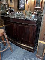 Front view of dark wood bar with marble top showing scratches and brass foot rail.