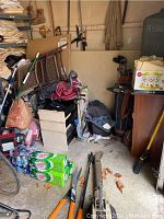 Photo showing assorted garden tools including blower, shears, pruner, crowbar, and bags stacked in garage corner.