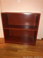 Front view of wooden bookcase showing two open shelves and reddish-brown finish, with visible scratches.
