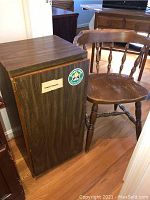 Photo showing side view of wooden cabinet with dark wood grain veneer and stickers next to wooden spindle-back chair