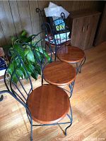Four wooden seat chairs with black metal decorative frame and backing, arranged in corner with a plant and other items nearby