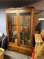 Front view of the wooden locking cabinet with two glass panel doors and two drawers at the bottom. Shows wood grain and some scratches.
