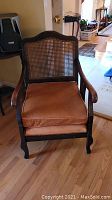 Front view of mahogany chair showing caned back and orange seat cushion, highlighting wood finish and condition.