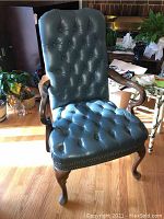 Front view showing the tufted blue leather upholstery on the chair back and seat, wooden curved armrests and legs.
