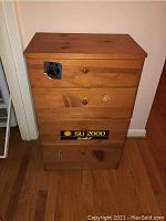 Full front view of medium wood chest of drawers with four drawers and stickers on front, showing wood grain and sticker details.