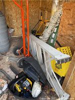 Photo showing orange dolly, aluminum ladder, black and yellow chainsaw case, and coiled hammock rope inside a shed.