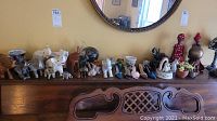 Wide view of the collection on a wooden dresser including elephants, figurines, miniature shoes, teacup, and ceramic vases