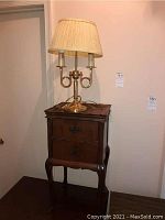 Brass lamp with three candle-like lights under beige fabric shade on top of the end table.