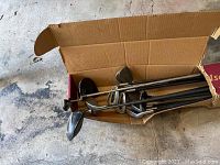 Photo showing several golf clubs in a cardboard box with visible club heads and shafts.
