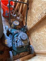 Yard Machines green lawn mower with black engine, orange bucket, and tools in background.