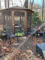 Four mesh outdoor chairs placed near a gazebo and patio area on a brick and leaf-covered floor.