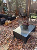 Overview of the two rectangular wicker coffee tables with glass tops on outdoor deck surrounded by fall leaves and outdoor furniture.