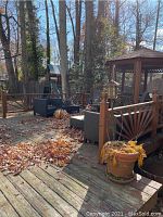 Wide view of a wood deck holding multiple planters, patio furniture and some dried leaves scattered around.