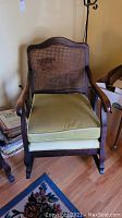 Full view of wooden rocking chair with caned back and detachable green cushion showing scratches and wood finish.