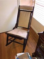Front view of vintage wooden rocking chair with beige upholstery on seat and backrest showing wood frame and fabric condition.