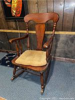Front view of wooden rocking chair with cushioned seat showing crack in wood and scratches.