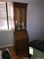Full view of tall wooden secretary with glass upper cabinet and mirrored doors, wooden lower bureau with drawers.
