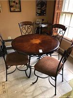 Photo showing entire kitchen table set with round wooden table and four metal framed chairs with cushioned seats.