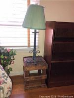 Wooden crate side table with green lampshade lamp on top, near window and bookshelf