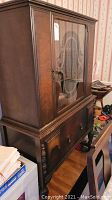 Side view of vintage wooden china cabinet showing glass door with oval etched design, drawer below and turned legs.