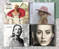 Four CD jewel cases with front covers showing Pink, Lady Gaga, Taylor Swift, and Adele albums.