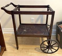 Front view of antique wooden tea trolley showing open top frame and stained bottom shelf.