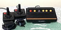 Atari Flashback console with two wired joysticks and power adapter all placed on a green cloth surface.