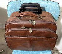 Top angle view of the brown leather wheeled briefcase showing the three zippered compartments and handle.