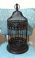 Full view of the decorative black metal bird cage with domed top, placed on a blue chair.