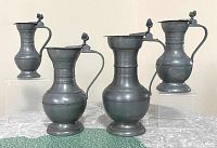 Front view showing four vintage pewter pitchers with double acorn lid finials in various heights
