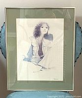 Full view of the framed lithograph showing the woman sitting with curly hair, soft shading, and muted colors under glass with visible artist signature.