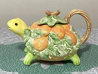 Side view of vintage Fitz Floyd turtle ceramic teapot showing yellow turtle head and detailed orange fruit and green leaves on shell.