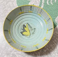Top view of light blue ceramic bowl with yellow rim and black and yellow floral and tree-like motifs inside