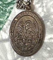 Close-up front view of the oval sterling silver pendant with Saint Michael relief and text.