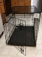 Metal foldable dog cage with black plastic tray floor, door open showing latch