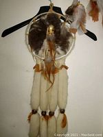 Large dreamcatcher hanging on wall with brown, white, and orange feathers and wooden beads.