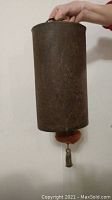 Side view of cylindrical metal gong held by top handle showing overall size and shape