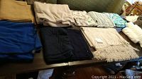 Photo showing various folded towels mostly in brown, white, and blue shades along with dark colored blankets on table