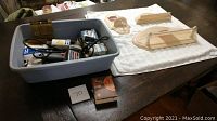 Overview of the plastic tub with drill and nails next to three unfinished wooden bath decor accessory pieces laid on a white towel.