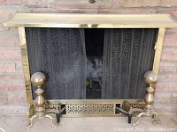 Full view of fireplace cover with brass/gold frame including mesh closing screens and andirons positioned in front.